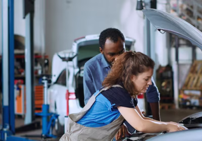 female mechanic working on car engine while a customer watches